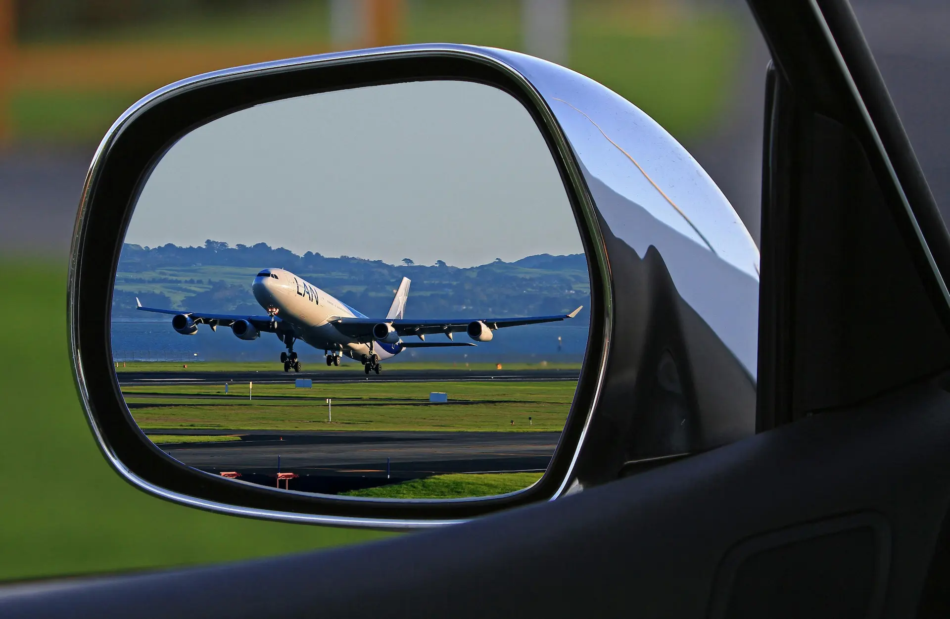 A car side mirror reflecting a plane taking off.
